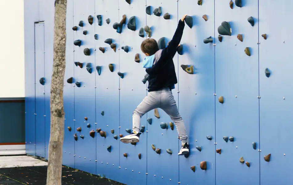 Ein Junge klettert an den Griffen einer künstlichen Kletterwand.