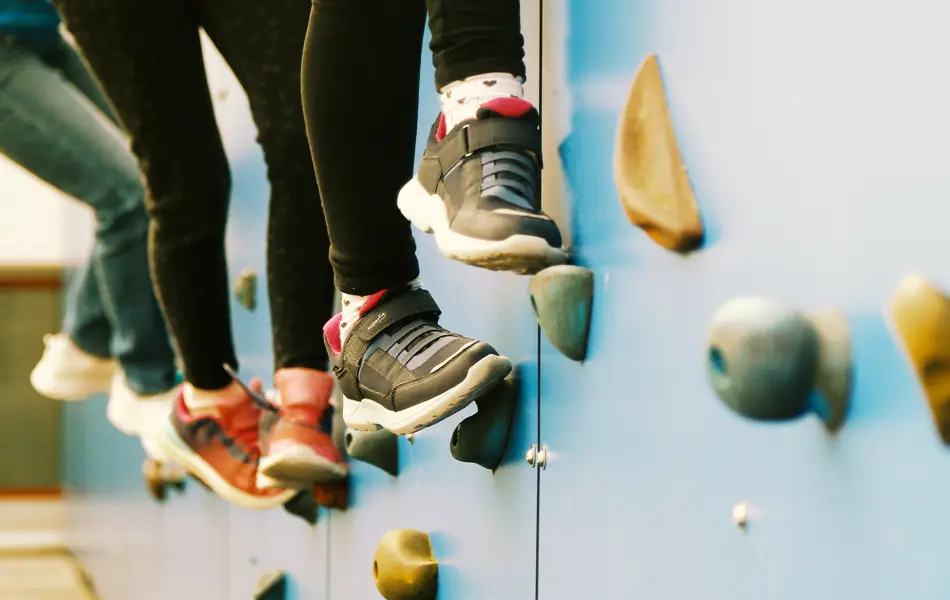 Kinderfüße stehen auf Tritten einer künstlichen Kletterwand.