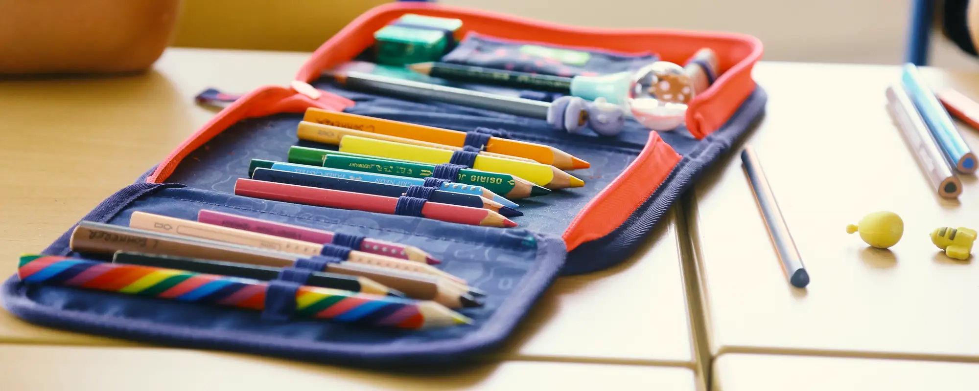 Auf der Schulbank liegt ein geöffnetes federmäppchen mit Buntstiften.