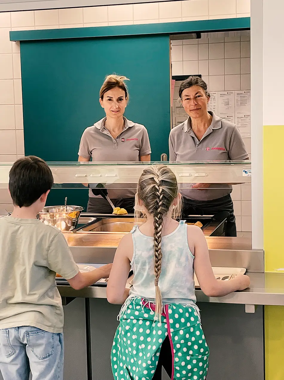 2 Kinder stehen vor der Essensausgabe in der Grunschule Zeitlarn.