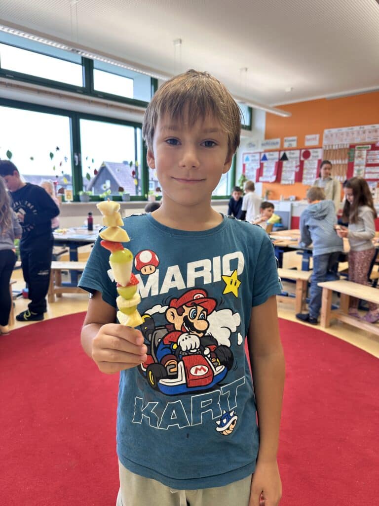 Ein Schüler zeigt stolz seinen fertigen Obstspieß.