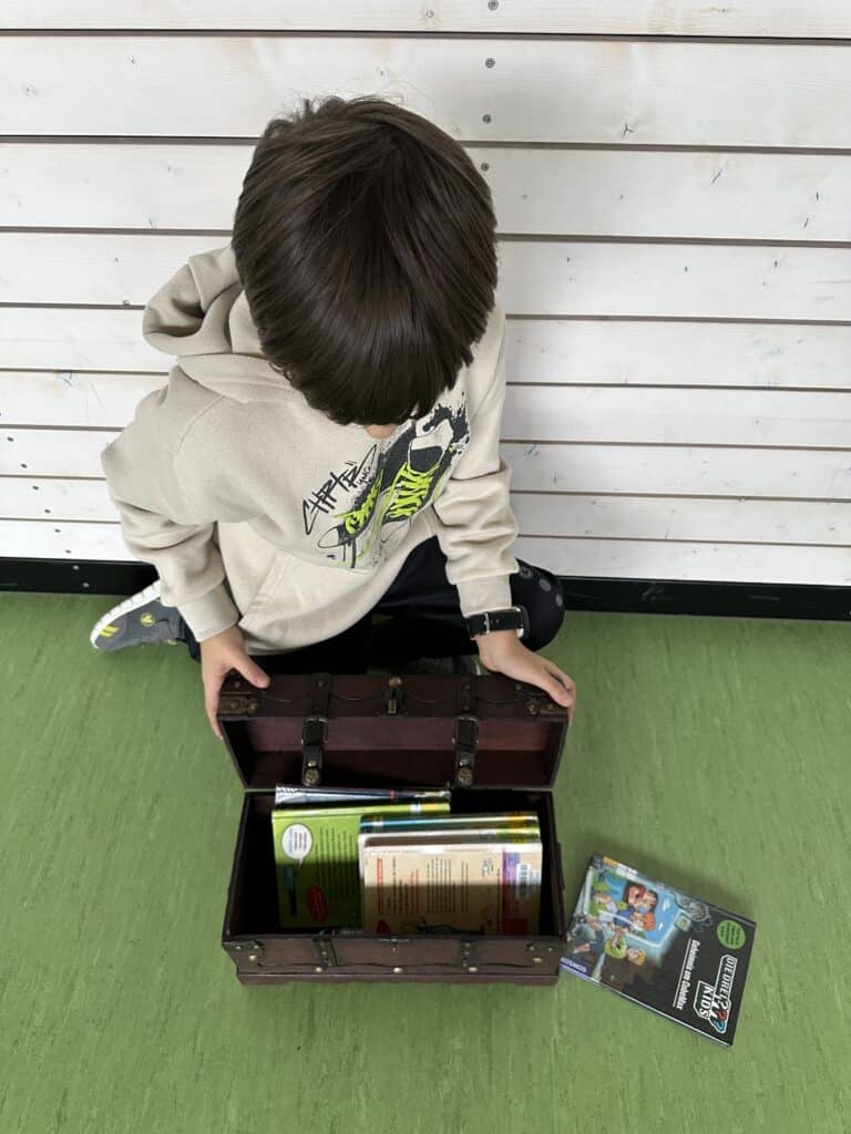Ein Schüler sitzt auf dem Boden mit einer Schatztruhe voller Bücher.